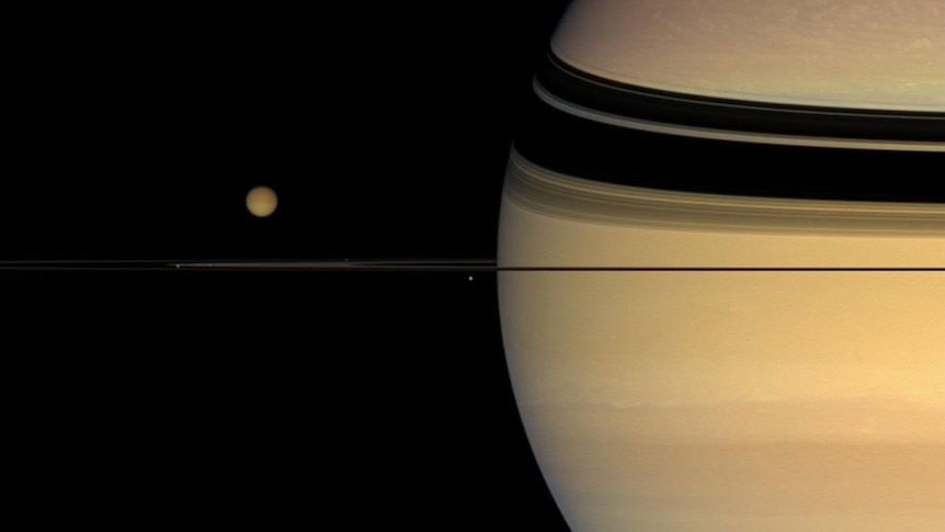 Saturn, taking up the right-hand half of the photo, with its rings extending to the left and two moons visible.