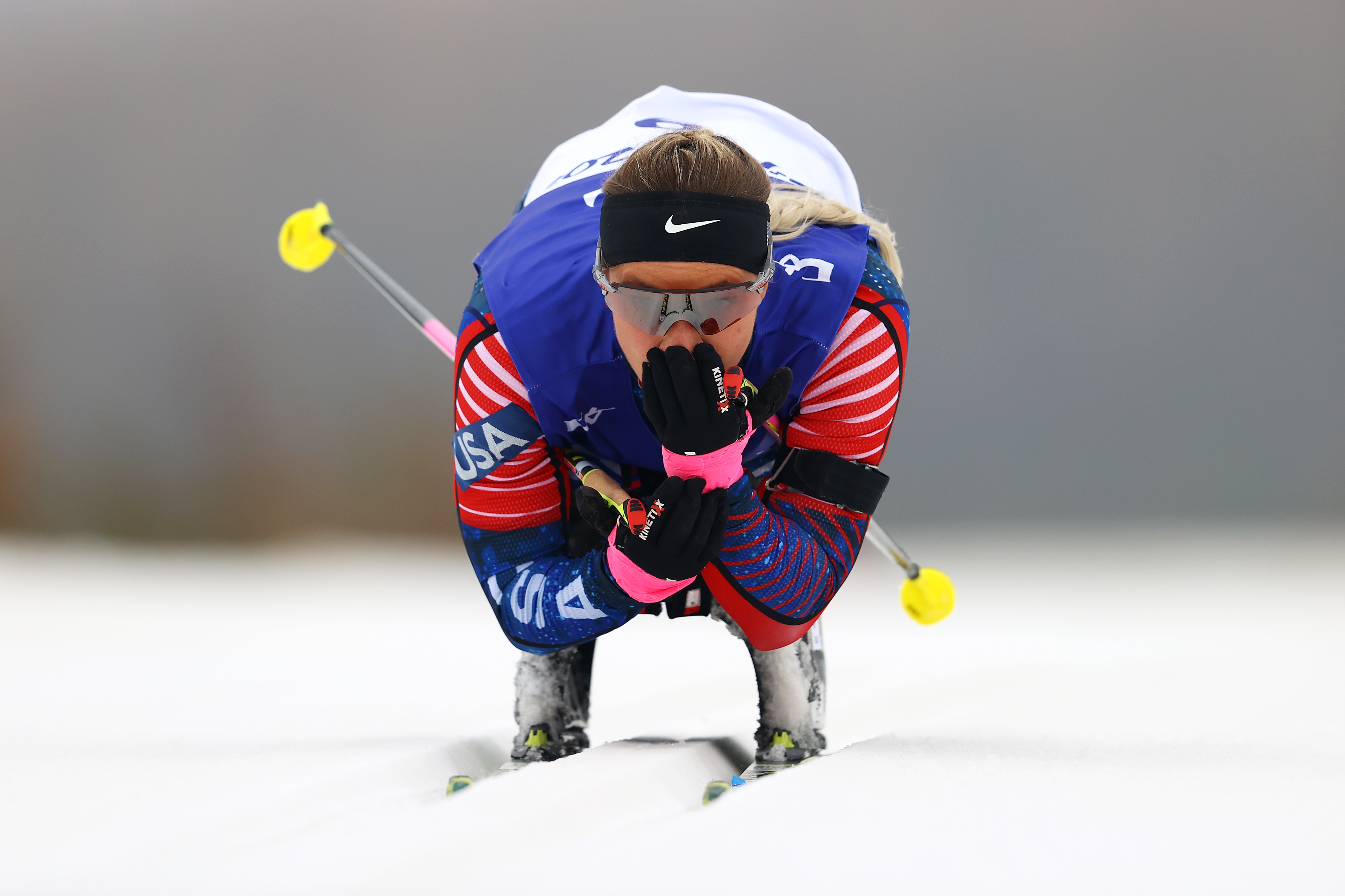 Uma mulher se inclina para a frente em seu esqui, olhando para frente, ela segura os bastões de esqui debaixo dos braços.