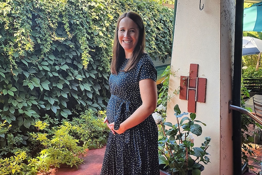 Jacinta wearing a green dress and smiling while pregnant.