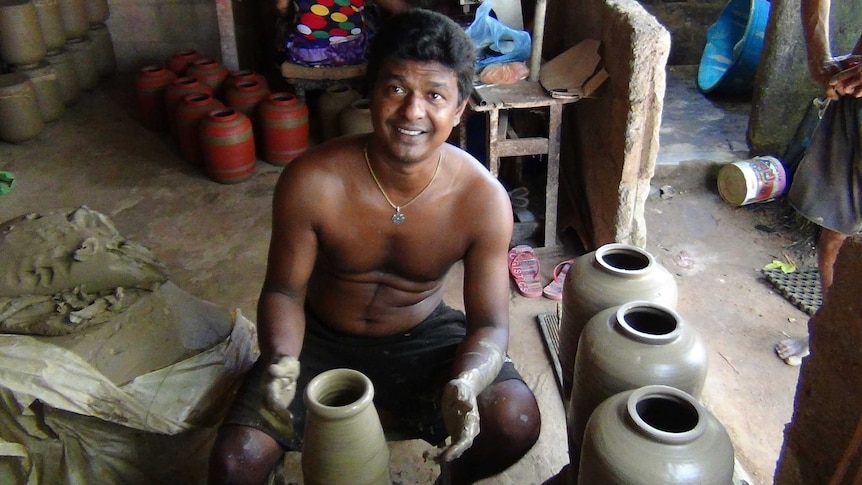 A Sri Lankan potter sits on the floor hand-making clay pots