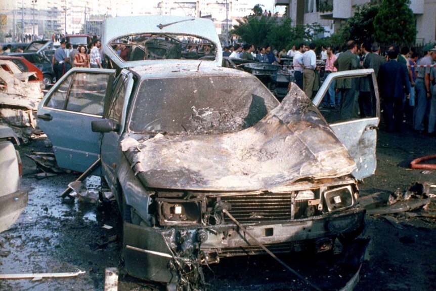 The shell of an exploded car sits in a busy Sicilian street.