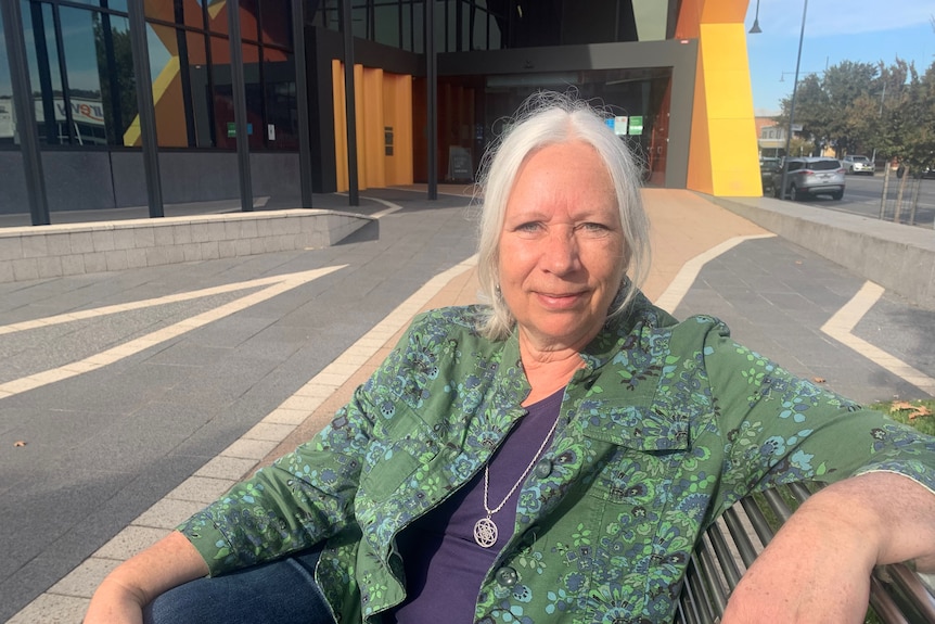 A woman sits on a bench in front of the Albury library. 