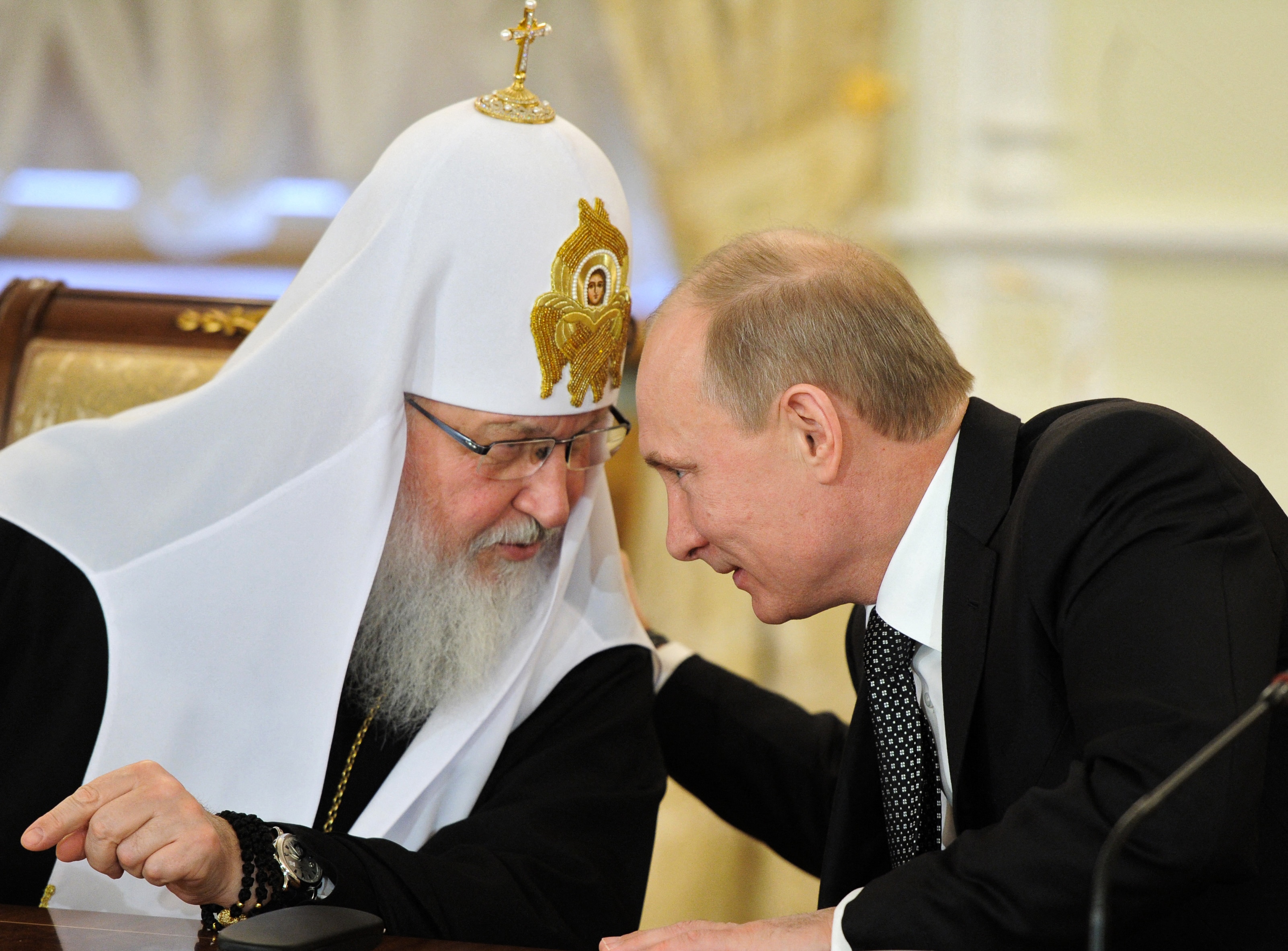 Vladimir Putin leans over to talk and put an arm around Patriarch Kirill, who is wearing an ornate watch on one wrist