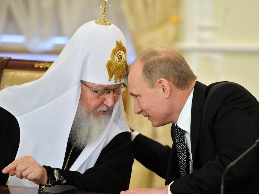 Vladimir Putin leans over to talk and put an arm around Patriarch Kirill, who is wearing an ornate watch on one wrist