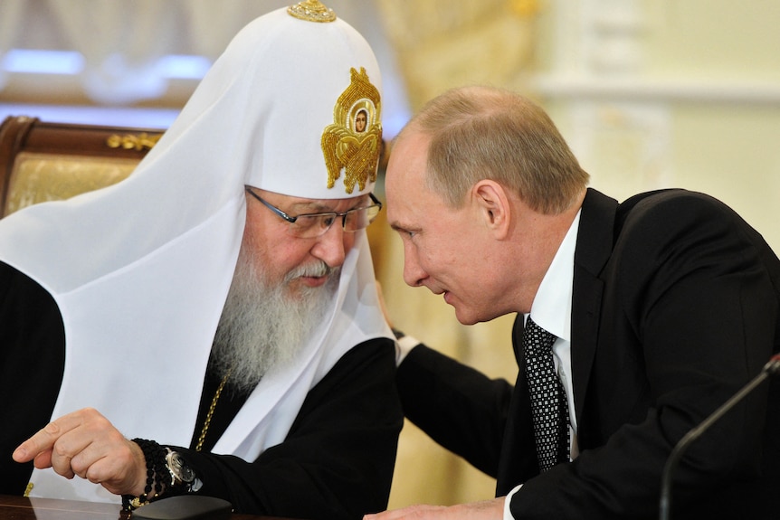 Vladimir Putin leans over to talk and put an arm around Patriarch Kirill, who is wearing an ornate watch on one wrist