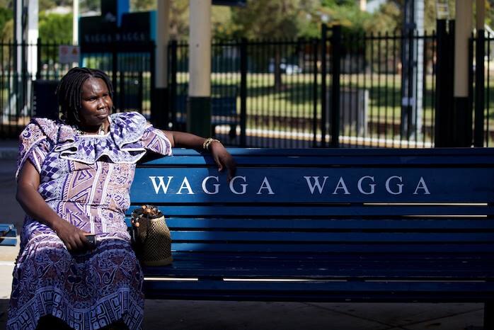 Constance sits at the Wagga Wagga train station, on a seat with the label 'Wagga Wagga'