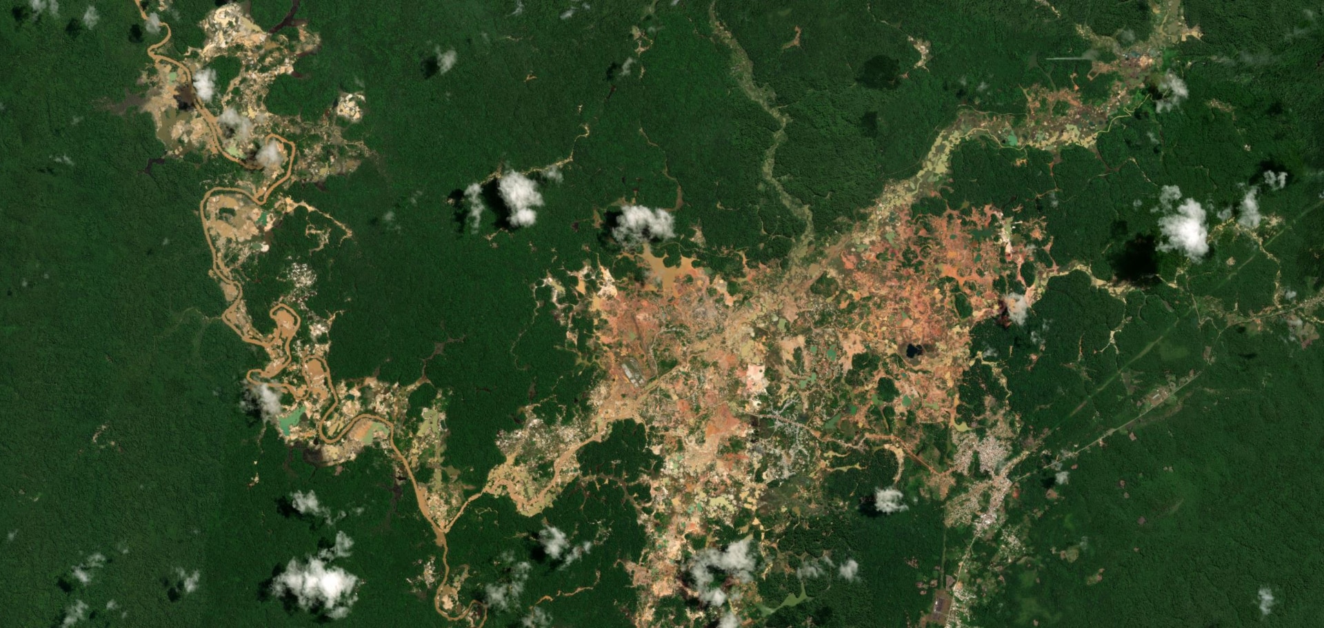 A sprawling orange-brown patch of mining land seen amid solid green Amazon forestry, seen from above.
