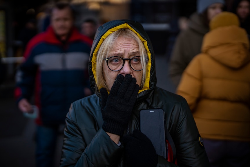 A woman in a rain jacket covers her mouth in shock on the streets of Kyiv.