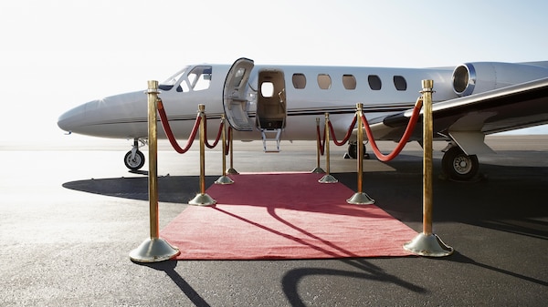 A white small plane sits on the tarmac with a red carpet leading to its door.