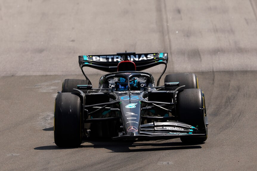 George Russell driving his Mercedes F1 car, which is leaning to the right because it is broken after hitting a wall.