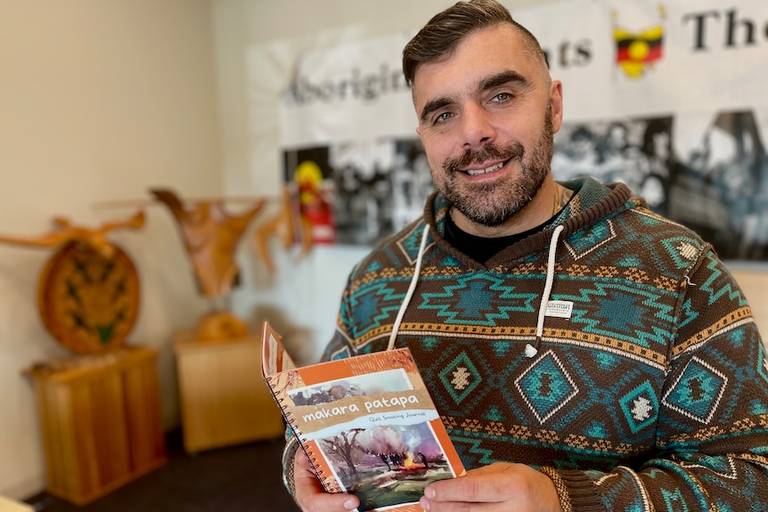A man holds a quit smoking booklet in front of a sign about Indigenous culture.