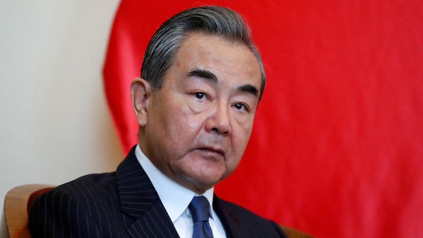 Wang Yi wears a suit as he sits down in front of a red background.