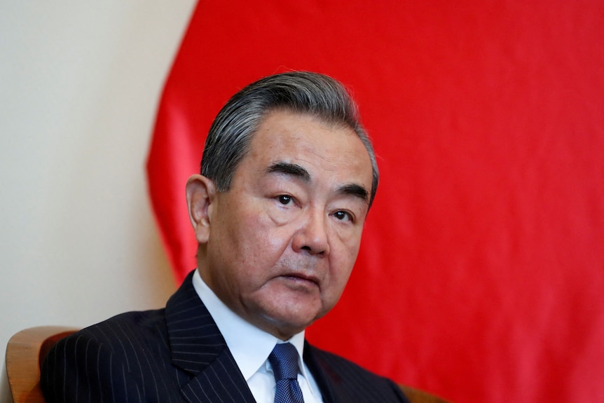 Wang Yi wears a suit as he sits down in front of a red background.