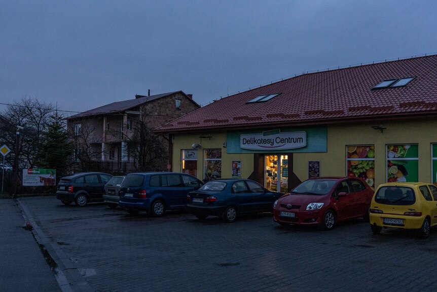 Cars parked outside a supermarket. A light from inside stands out against the dark sky
