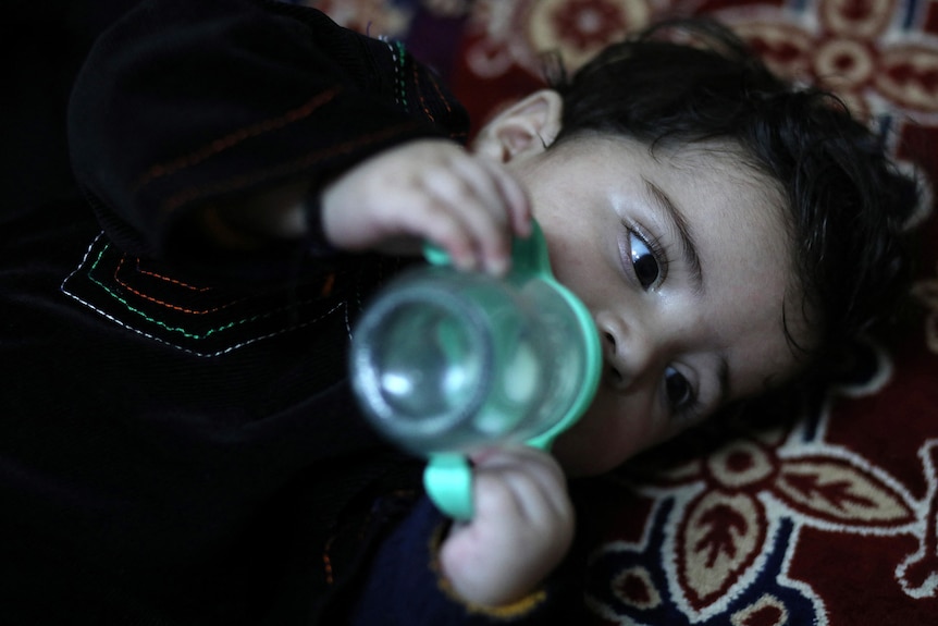Baby Sohail drinks from a milk bottle outside Hamid Safi's house, January 7, 2022.