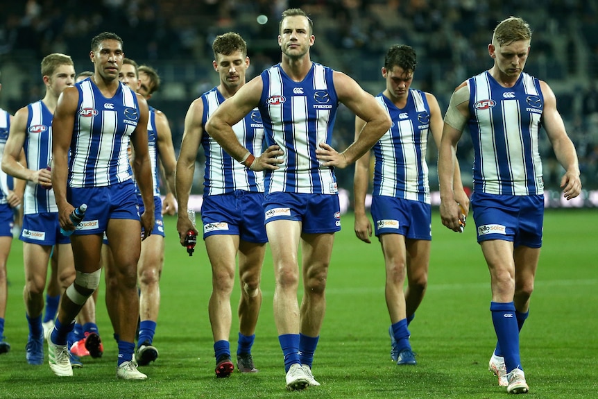 A group of North Melbourne AFL players walk off the field after losing to Geelong.