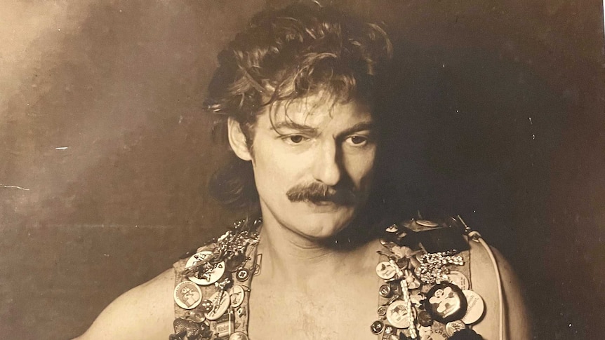 A black and white portrait of Ivor Cole in the 1980s, in his iconic punk vest covered in badges.