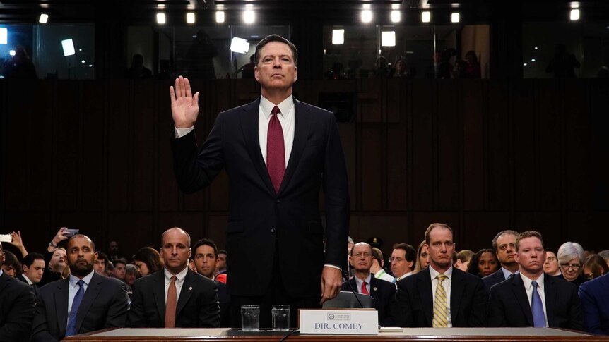 James Comey holds one hand in the air as he is sworn in prior to Senate testimony.