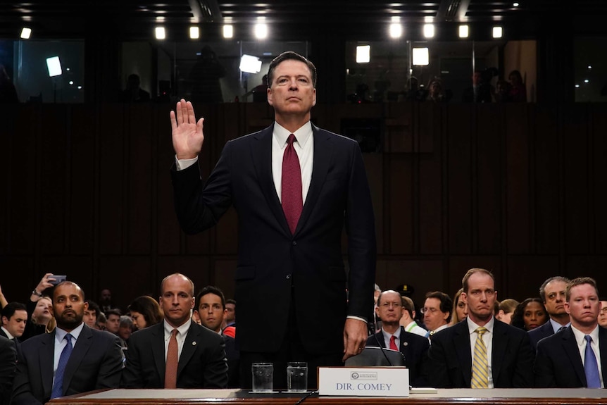 James Comey holds one hand in the air as he is sworn in prior to Senate testimony.