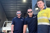 Three auto-electricians wearing company attire and sunglasses standing outside their workshop.