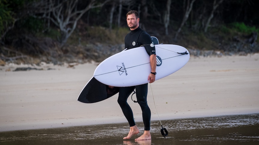 Chris Hemsworth carries surfboards on the beach at Byron Bay
