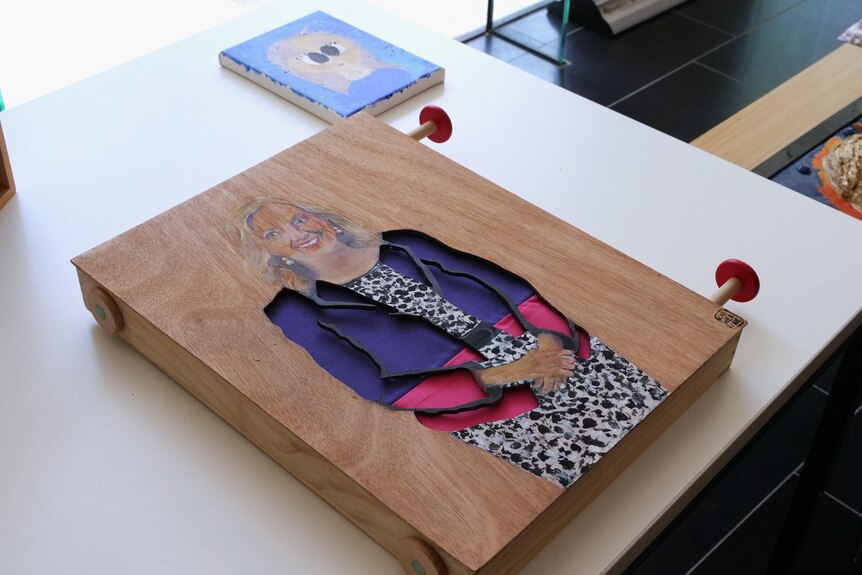 A painted wooden block carving of a blonde-haired woman in a blazer. Knobs are attached to the side of the wood.