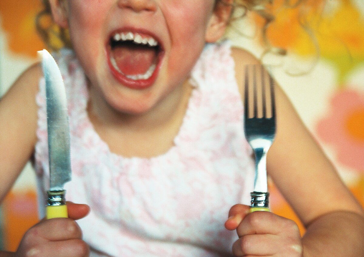 A child bangs her knife and fork on the table and yells.
