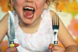 A child bangs her knife and fork on the table and yells.