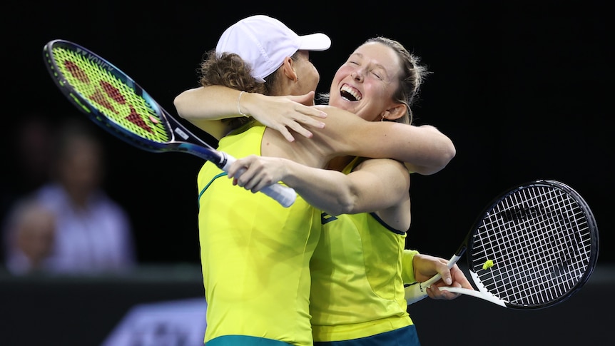 Two Australian women's tennis players embrace in mid-court after a win, with the player on the right wearing a huge smile.