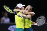 Two Australian women's tennis players embrace in mid-court after a win, with the player on the right wearing a huge smile.