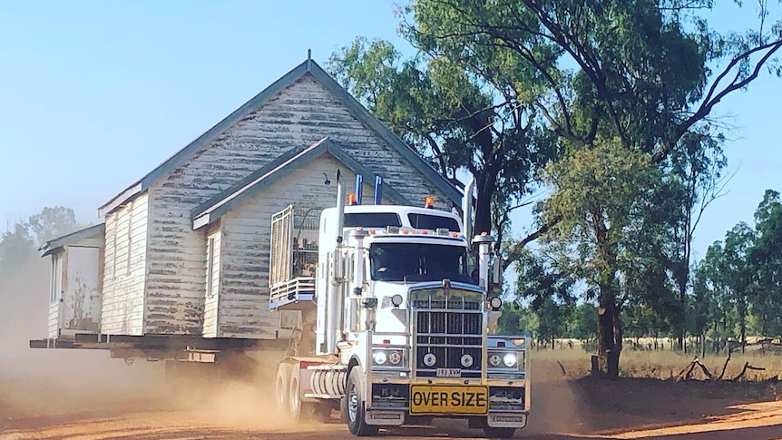 A church on the back of a truck being driven on a dusty dirt road.