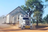 A church on the back of a truck being driven on a dusty dirt road.