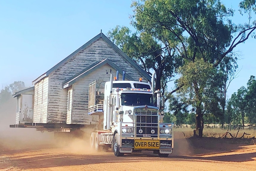A church on the back of a truck being driven on a dusty dirt road