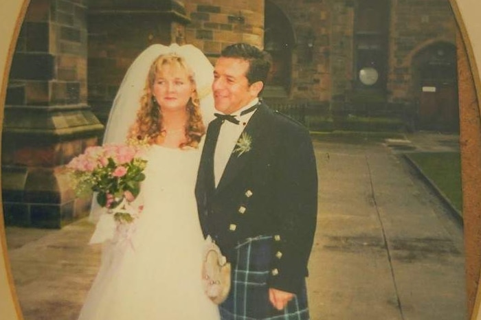 An old photo frame with a picture of a woman in a wedding dress smiling next to a  man in a kilt and suit jacket with bowtie.