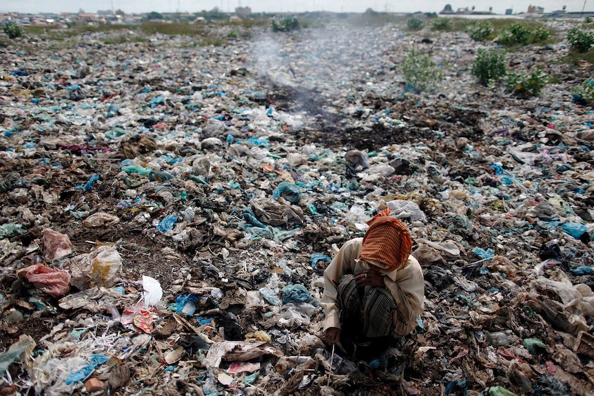 An elderly woman bends searches through rubbish on the ground