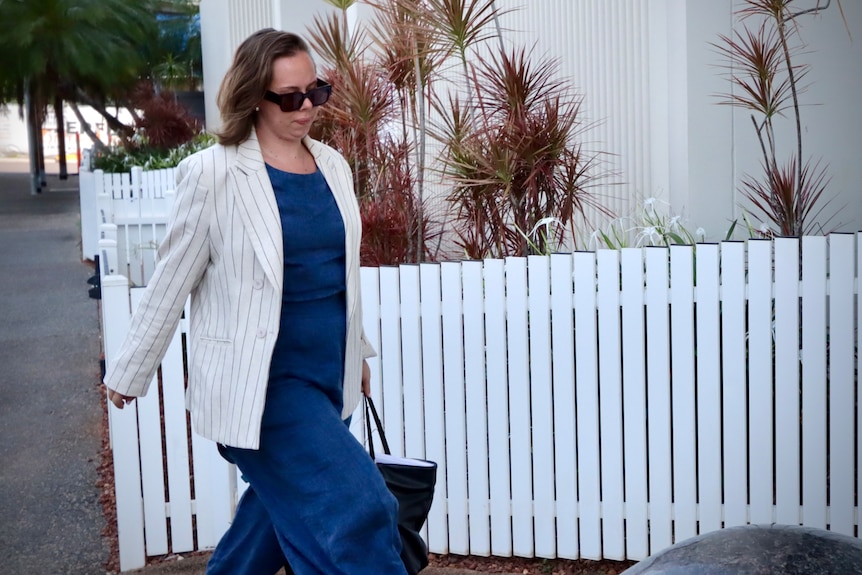 a woman wearing a blue dress and white blazer on her way to court