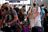 People wearing face masks line up for check in at an airport