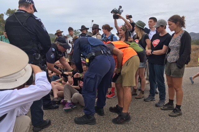 Queensland police pick up protesters who are sitting on the road while others watch on and media film the arrests.