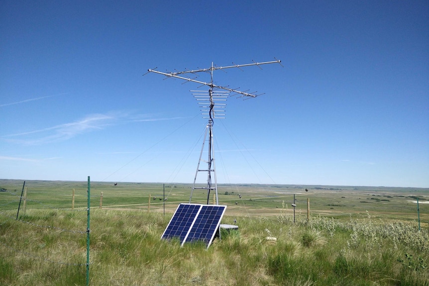 An antenna and solar panel in a green pasture.