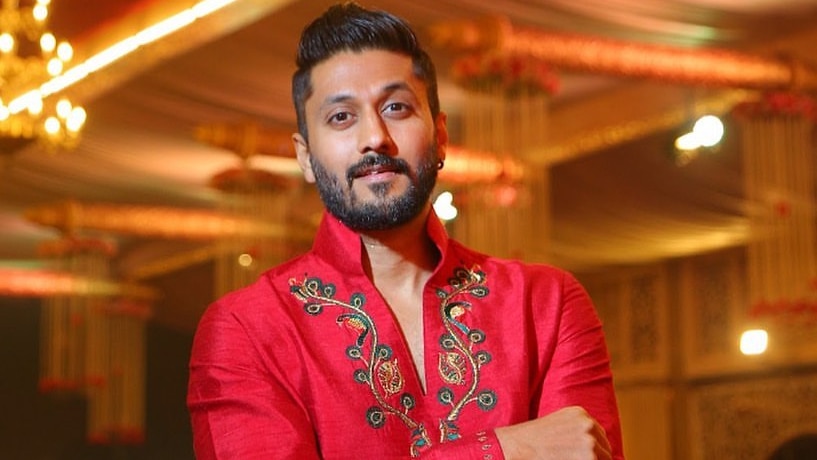 Chetan Kumar Ahimsa wearing a red shirt staring at the camera with his arms folded