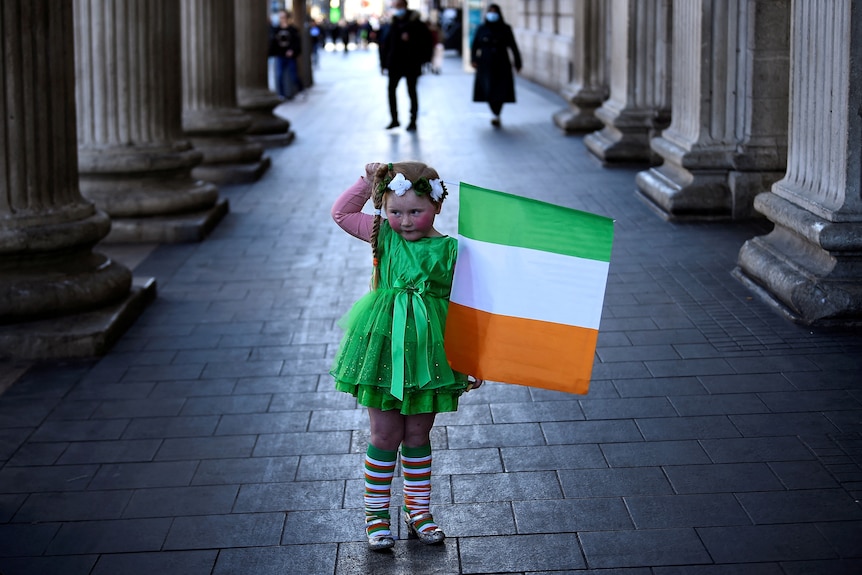 A girl in green dress holding an Irish flag. 