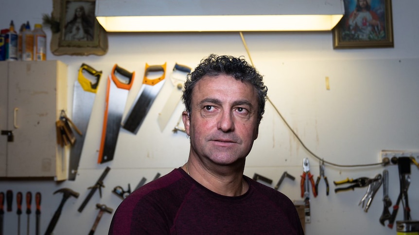 A man with curly hair stands in front of hanging tools.