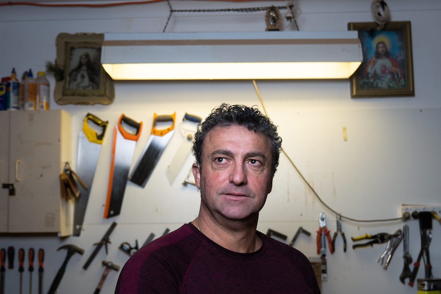 A man with curly hair stands in front of hanging tools.
