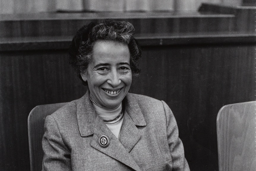 A black and white photo of a woman with short hair, smiling, wearing a collared coat