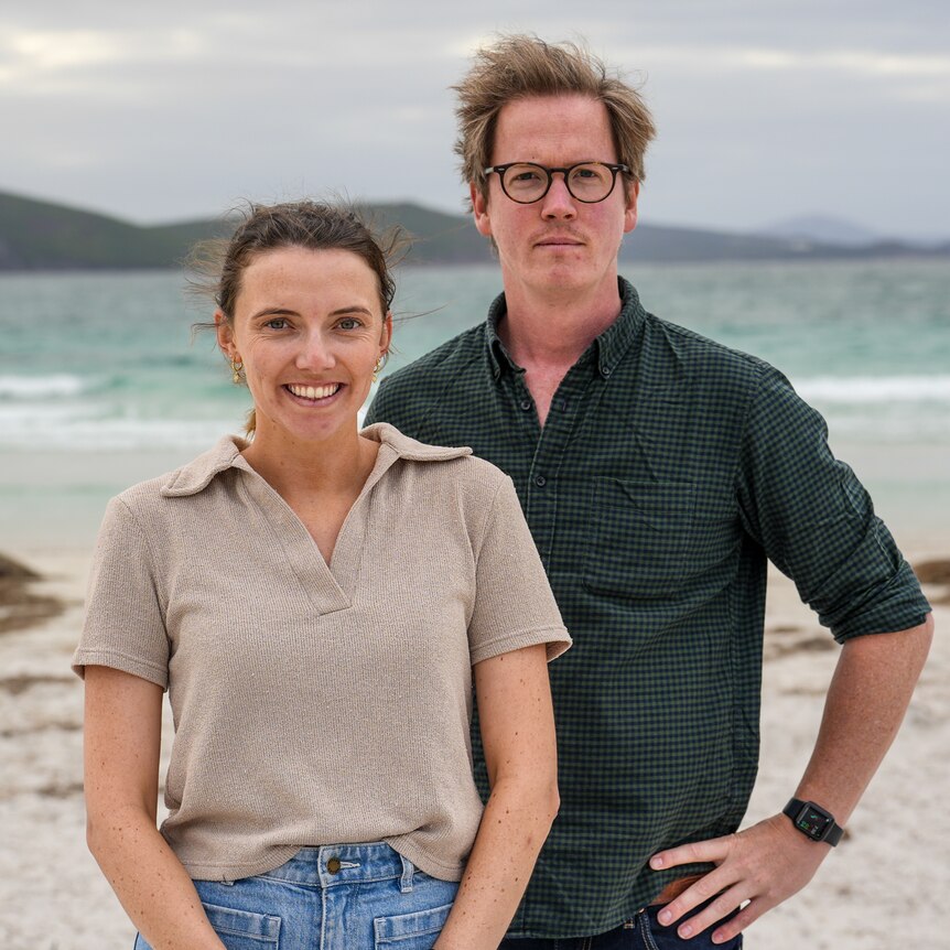 Kate Forrester and Andrew Chounding standing on a beach on a grey, windy day.