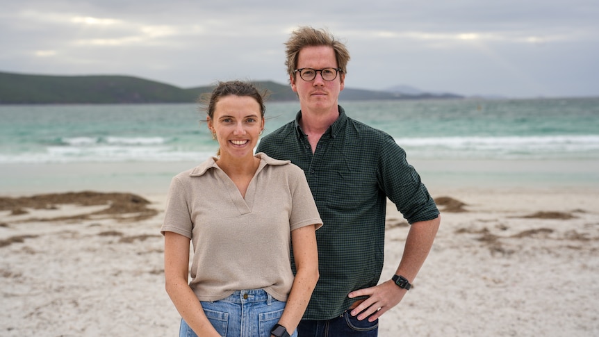 Kate Forrester and Andrew Chounding standing on a beach on a grey, windy day.
