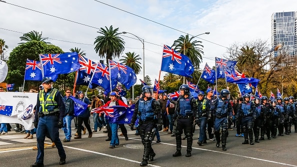 Marching protesters, surrounded by police, wave Australian flags
