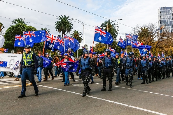 Marching protesters, surrounded by police, wave Australian flags