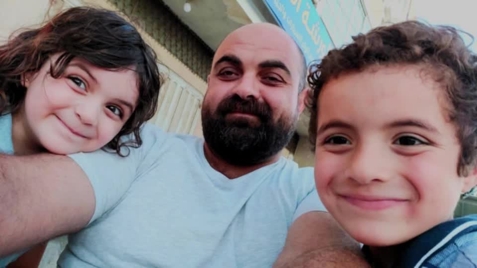 A bald man with a dark beard smiling in a selfie alongside a young boy and girl also smiling