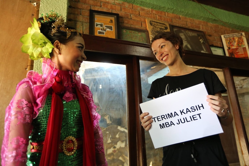 Juliet Burnett holds a sign saying "terima kasih mba Juliet", while smiling at a woman wearing Indonesian dress. 
